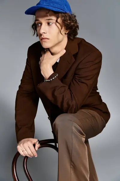 A stylish young man in a brown suit and blue baseball cap showcases his unique flair in an artistic studio. — Stock Photo