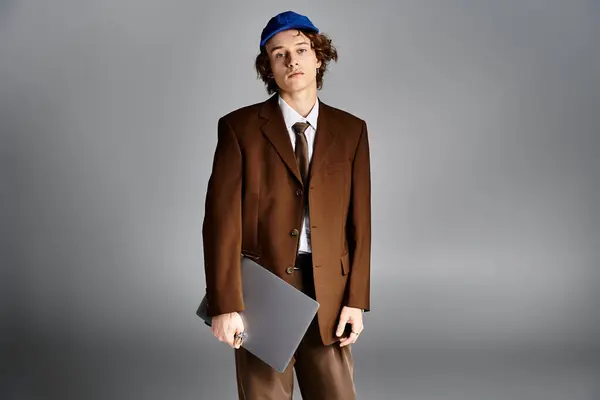 A stylish young man stands confidently in a studio, dressed in a brown suit paired with a baseball cap. — Stock Photo