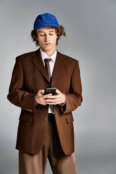 Ein stilvoller junger Mann in braunem Anzug und blauer Mütze greift in einem eleganten Studio zum Handy. — Stockfoto