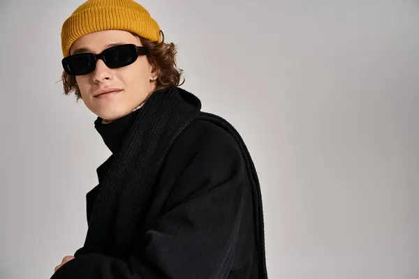 Questo individuo sicuro di sé mette in mostra un cappotto nero chic e un berretto giallo brillante in un ambiente elegante studio. — Stock Photo