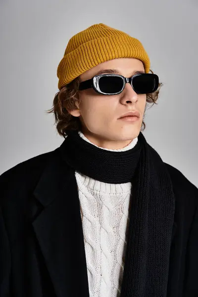 Un giovane alla moda con un cappotto nero e un berretto giallo trasuda fiducia in un ambiente da studio. — Foto stock