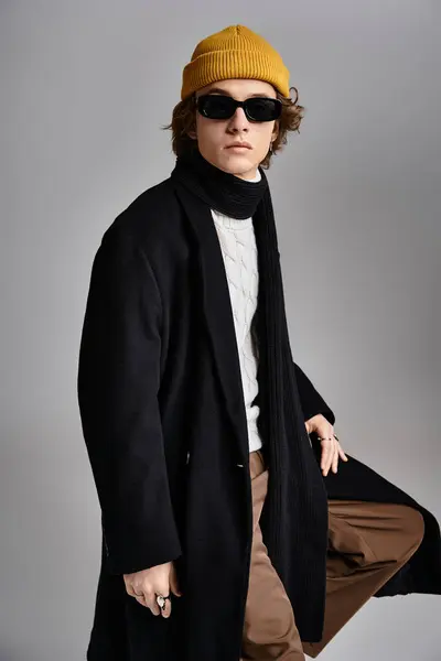 Dressed in a black coat and a cheerful yellow beanie, a young man exudes confidence in a chic studio. — Stock Photo