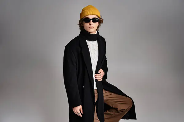Un beau jeune homme met en valeur la mode contemporaine avec un bonnet jaune et un élégant manteau noir dans un studio. — Photo de stock