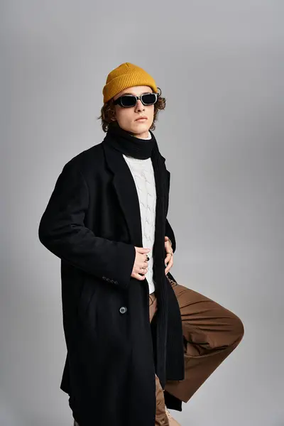 Un bel giovane uomo si erge con stile, indossa un cappotto nero e un vibrante berretto giallo, in mostra la moda moderna. — Foto stock