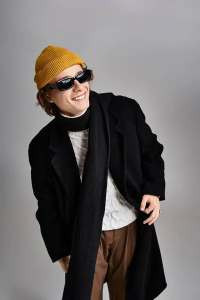 A handsome young man sports a black coat and yellow beanie, radiating charm in a stylish studio setup. — Stock Photo