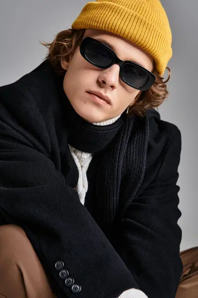 A young man exudes charm in a black coat and yellow beanie, showcasing a trendy look in a studio atmosphere. — Stock Photo