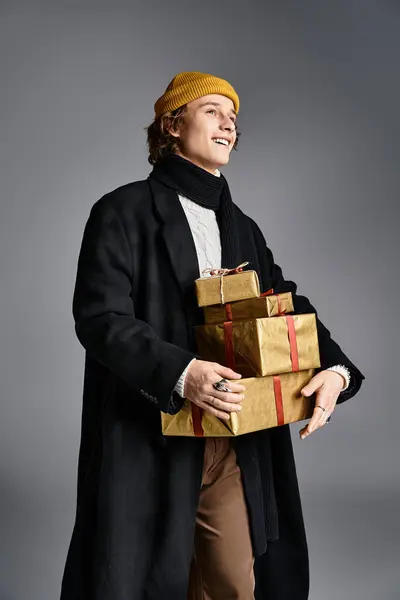 In a stylish studio, a young man in a yellow beanie carries wrapped presents. — Stock Photo