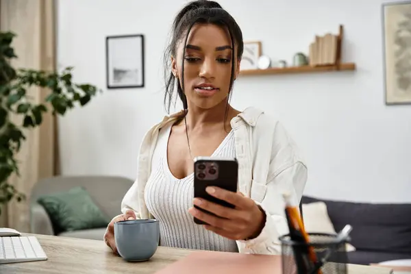 A young woman is studying from her cozy home, sipping coffee and checking her phone. — Stock Photo