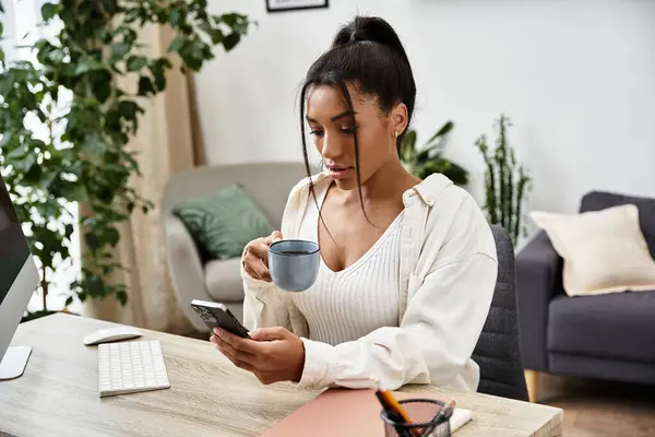 A dedicated young woman studies at home, enjoying coffee while engaging with her smartphone. — Foto stock