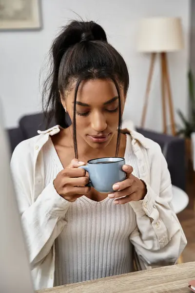 A young woman is focused on her remote studies while sipping coffee in her home space. — Stock Photo