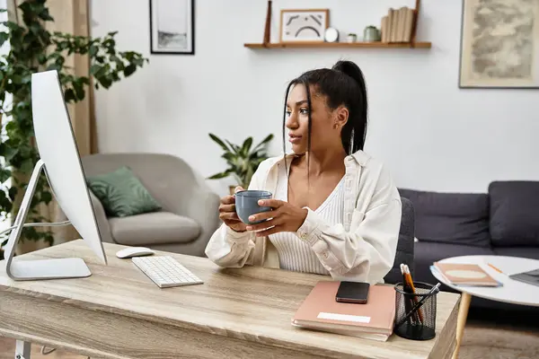 Eine fokussierte junge Frau studiert online und hält eine warme Tasse Kaffee in ihrem ruhigen Home Office. — Stockfoto