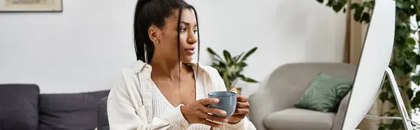 Eine junge Frau studiert von zu Hause aus, nippt am Kaffee und konzentriert sich auf ihre Arbeit in einer gemütlichen Umgebung. — Stockfoto