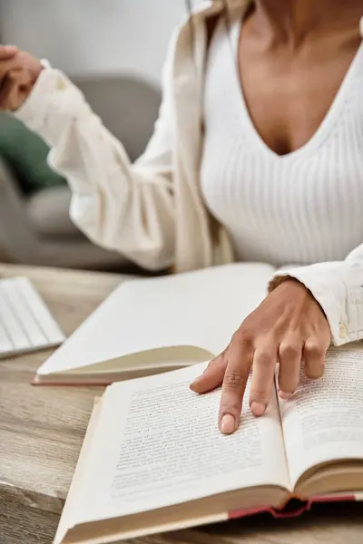 Молодая женщина усердно учится дома, переворачивая страницы в своей книге в окружении технологий. — стоковое фото