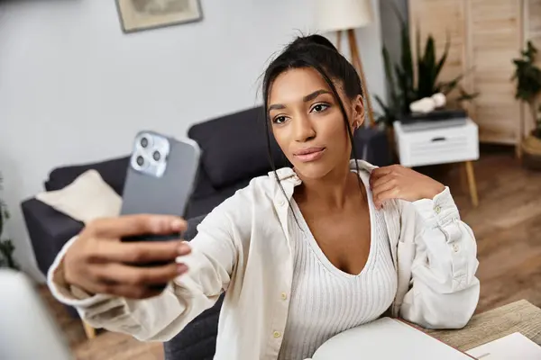 A young woman studies from home, capturing a moment with her smartphone while focused. — Stock Photo