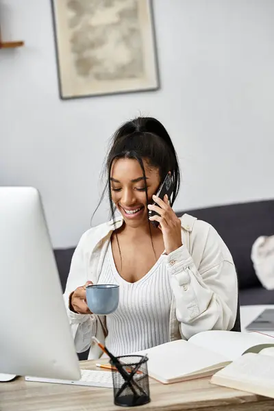 Eine junge Frau nimmt lächelnd am Fernlernen zu Hause teil, nippt am Kaffee und telefoniert. — Stockfoto