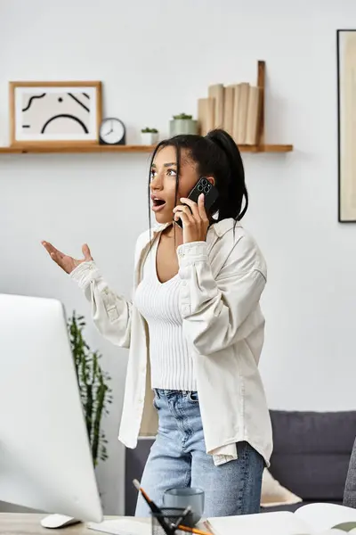 A surprised young woman studies at home, talking on the phone and gesturing enthusiastically. — Stock Photo