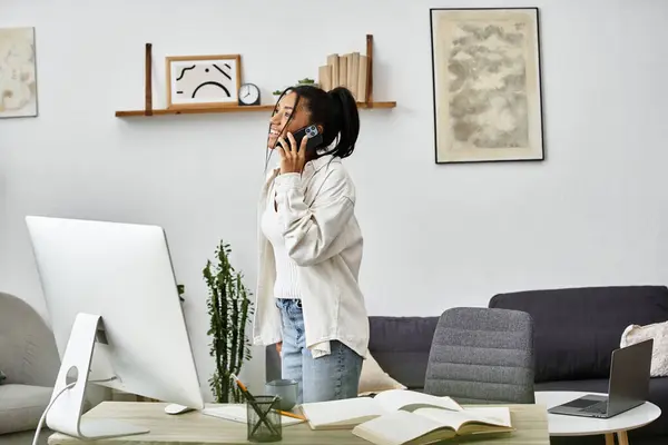 A young woman stands in her stylish home workspace, studying and talking on the phone. — Stock Photo