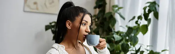 A beautiful young woman sips a warm drink as she focuses on her studies in her home. — Stock Photo
