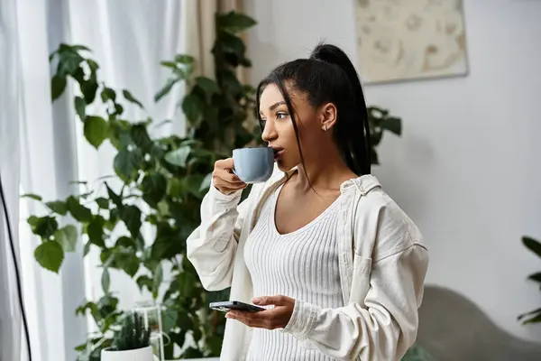 A beautiful young woman sips tea and studies, surrounded by lush indoor plants at home. — Stock Photo