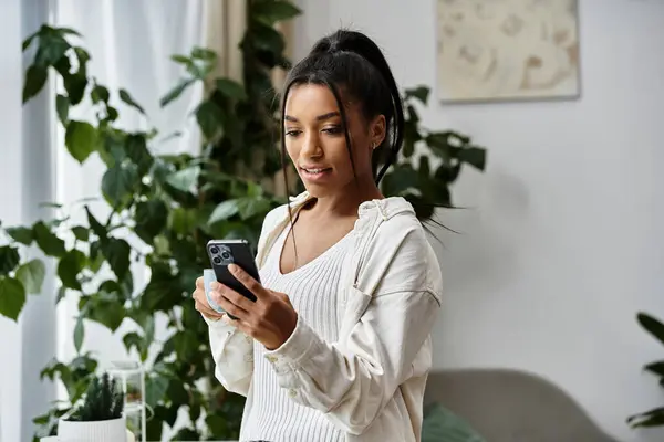 A young woman enjoys studying remotely, happily interacting with her smartphone in a tranquil room. — Stock Photo