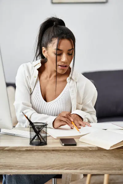 A young woman studies intently at her desk, taking notes and working from home with determination. — Stock Photo