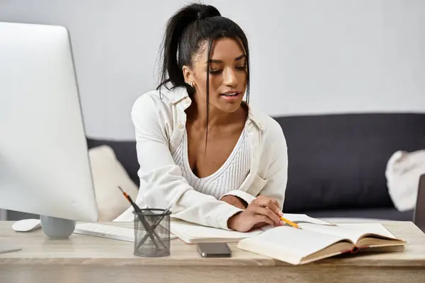 A young woman studies diligently from home, writing notes while using her computer. — Stock Photo