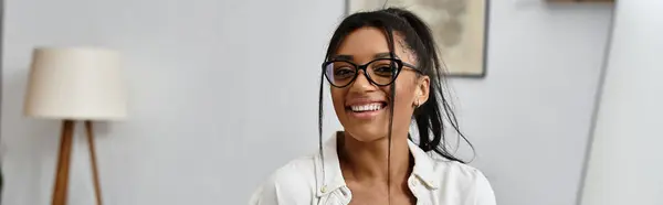 Una giovane donna che studia sorrisi a distanza mentre lavora nel suo accogliente ambiente domestico. — Foto stock