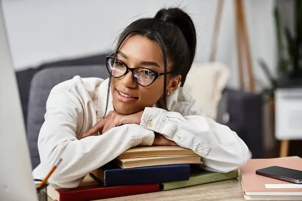 A young woman studies at home, surrounded by books and focused on her laptop with a smile. — Stock Photo