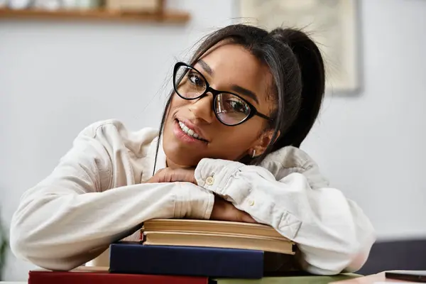 A young woman engaged in her studies, smiling while resting on a stack of books at home. — Stock Photo
