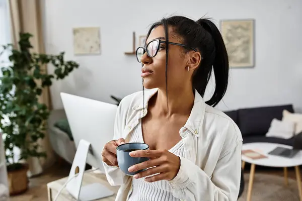 A beautiful young woman holds a coffee cup, focused on her studies in a peaceful home environment. — Stock Photo