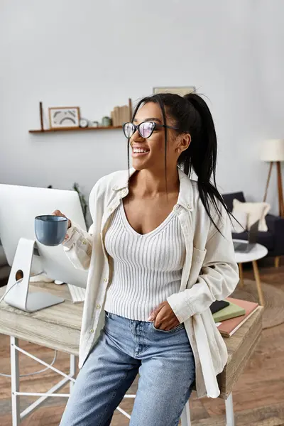 A cheerful young woman studies at home, holding a coffee mug and smiling while learning. — Stock Photo