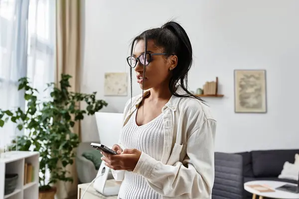 A young woman studies at home, focusing on her phone while surrounded by a warm atmosphere. — Stock Photo