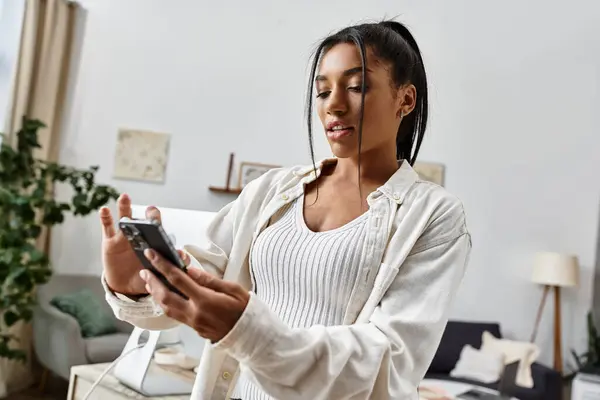 A beautiful young woman focused on her studies while using her smartphone at home. — Stock Photo