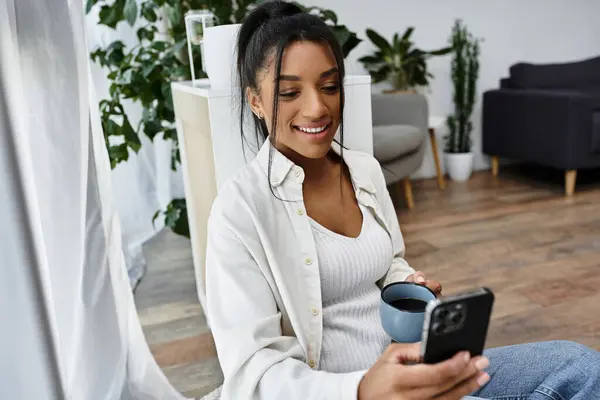 Brightly lit room features a woman enjoying remote study time with coffee and smartphone in hand. — Stock Photo