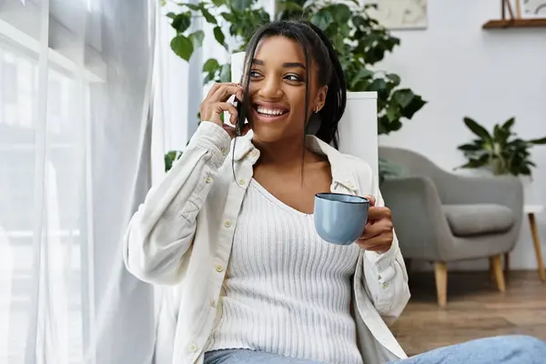 Una giovane donna allegra studia a distanza da casa sua, sorseggiando caffè e chiacchierando felicemente. — Foto stock