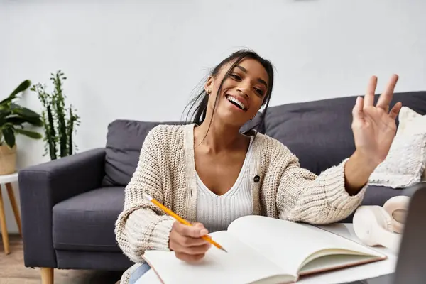 A young woman engages in remote studying at home, smiling and taking notes with enthusiasm. — Stock Photo