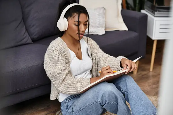 A beautiful young woman listens and takes notes while studying in her stylish living room. — Stock Photo