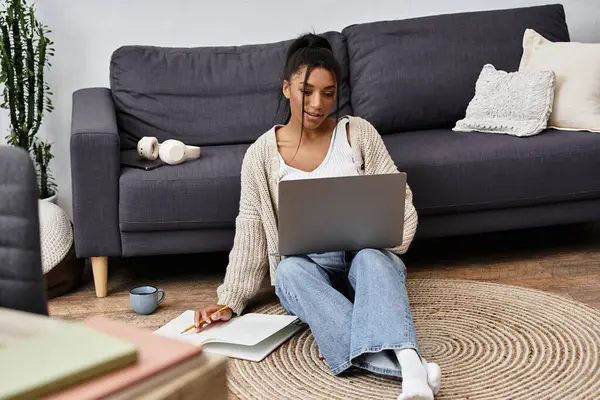 Eine junge Frau studiert bequem auf dem Fußboden, konzentriert auf ihren Laptop, während sie Notizen macht. — Stockfoto