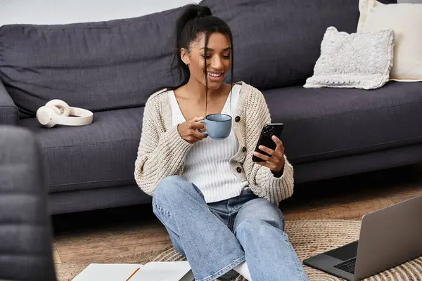 Eine junge Frau sitzt gemütlich auf dem Fußboden und hält während des Studiums eine Tasse Kaffee. — Stockfoto