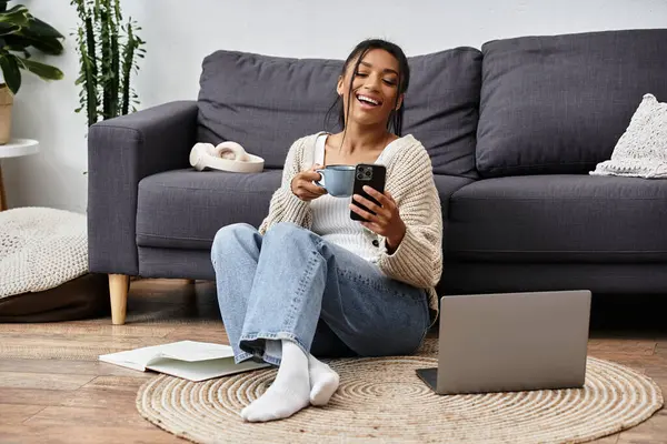 A young woman relaxes on the floor, studying with a laptop, coffee in hand, surrounded by comfort. — Stock Photo