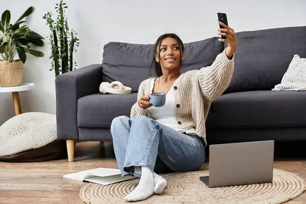 Auf dem Boden sitzend, genießt eine fröhliche Frau Kaffee und studiert, während sie ihren Laptop benutzt. — Stockfoto