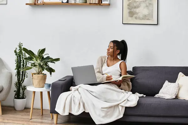 A beautiful young woman is immersed in her studies, seated on a couch at home. — Stock Photo
