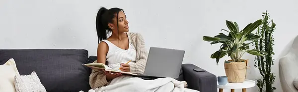 The young woman studies with a notebook and laptop in a cozy living space filled with plants. — Stock Photo