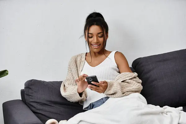 Eine schöne junge Frau sitzt gemütlich auf einer Couch und tippt während des Studiums mit ihrem Smartphone. — Stockfoto