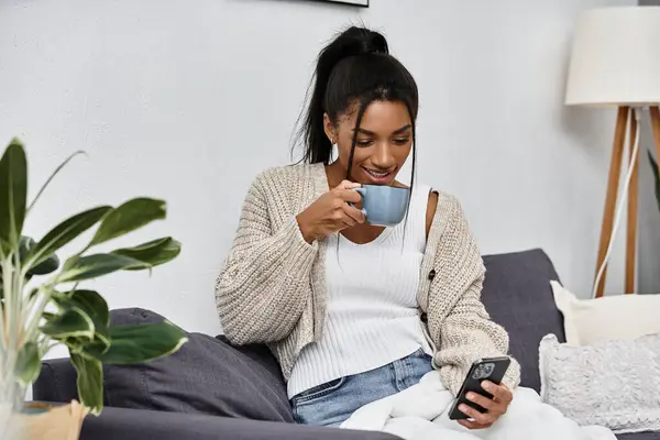 The woman sips her drink while engaged in remote studying on her smartphone at home. — Stock Photo