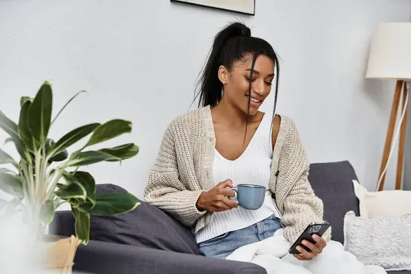 A beautiful woman relaxes at home, studying on her phone while sipping a warm beverage. — Stock Photo