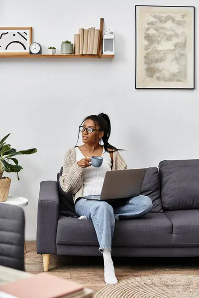 A young woman studies comfortably from her living room, holding a warm cup of coffee and smiling. — Foto stock