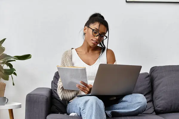 Eine junge Frau, die sich auf ihr Fernstudium konzentriert, sitzt gemütlich auf einem Sofa mit Laptop. — Stockfoto