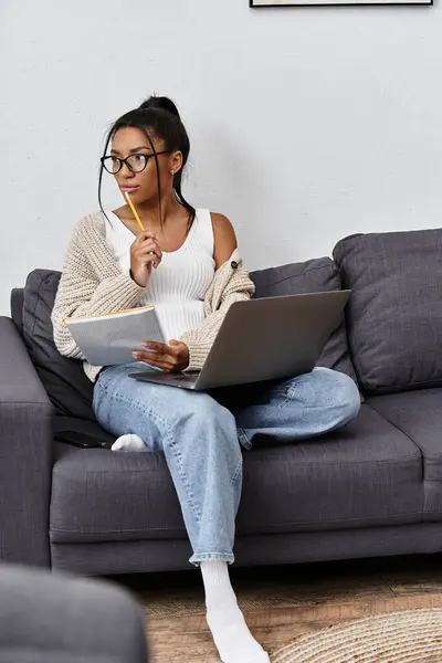 A jovem se envolve atenciosamente em estudos remotos, equilibrando seu laptop e notas. — Fotografia de Stock