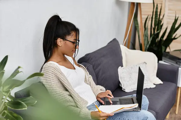 Engaged in remote learning, a young woman types on her laptop with notes beside her. — Stock Photo